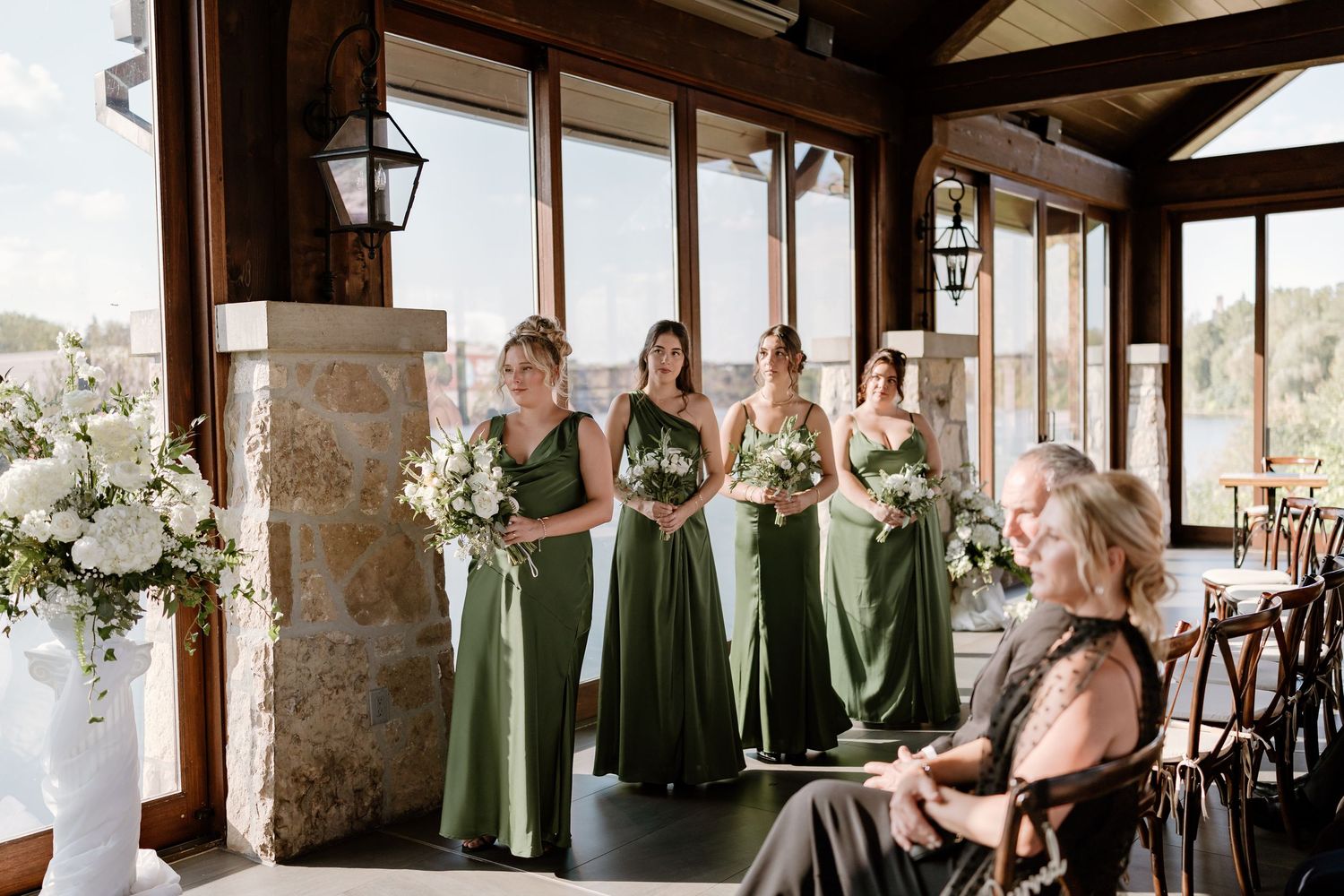 Bridesmaids in sage green dresses standing in elegant venue with stone pillars.