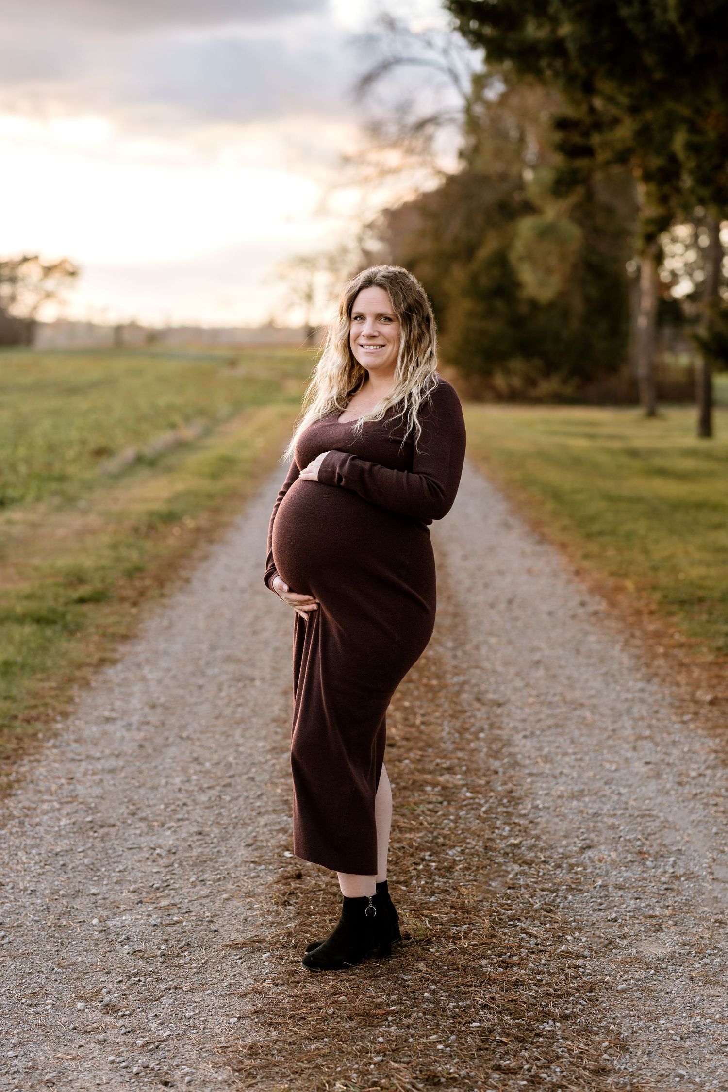 Maternity photos on a gravel path showing person in brown dress during golden hour.