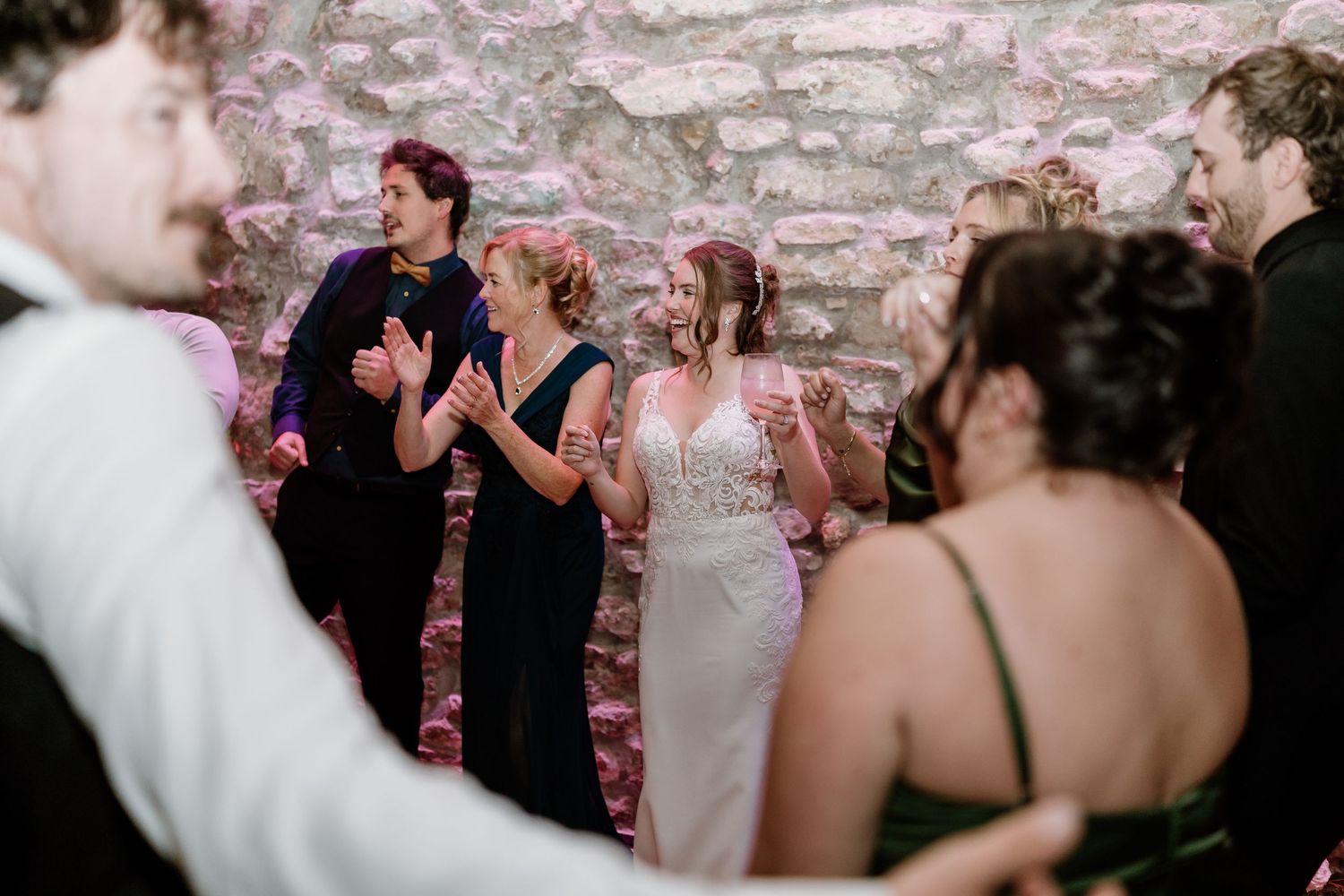 Wedding party dancing and celebrating in venue with pink ambient lighting.