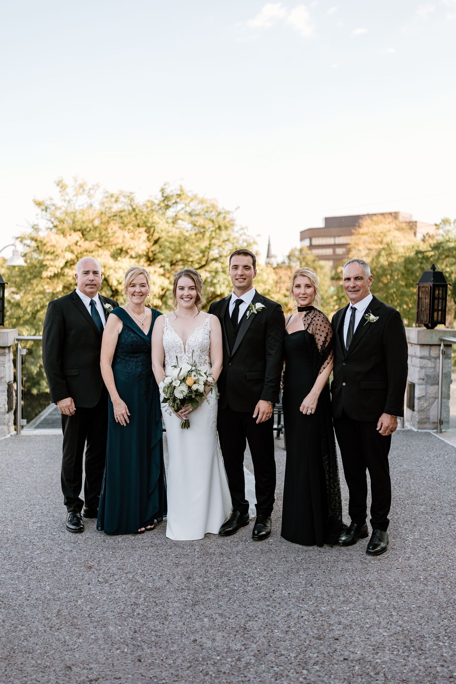 Elegant wedding party in formal attire poses on outdoor terrace at sunset.
