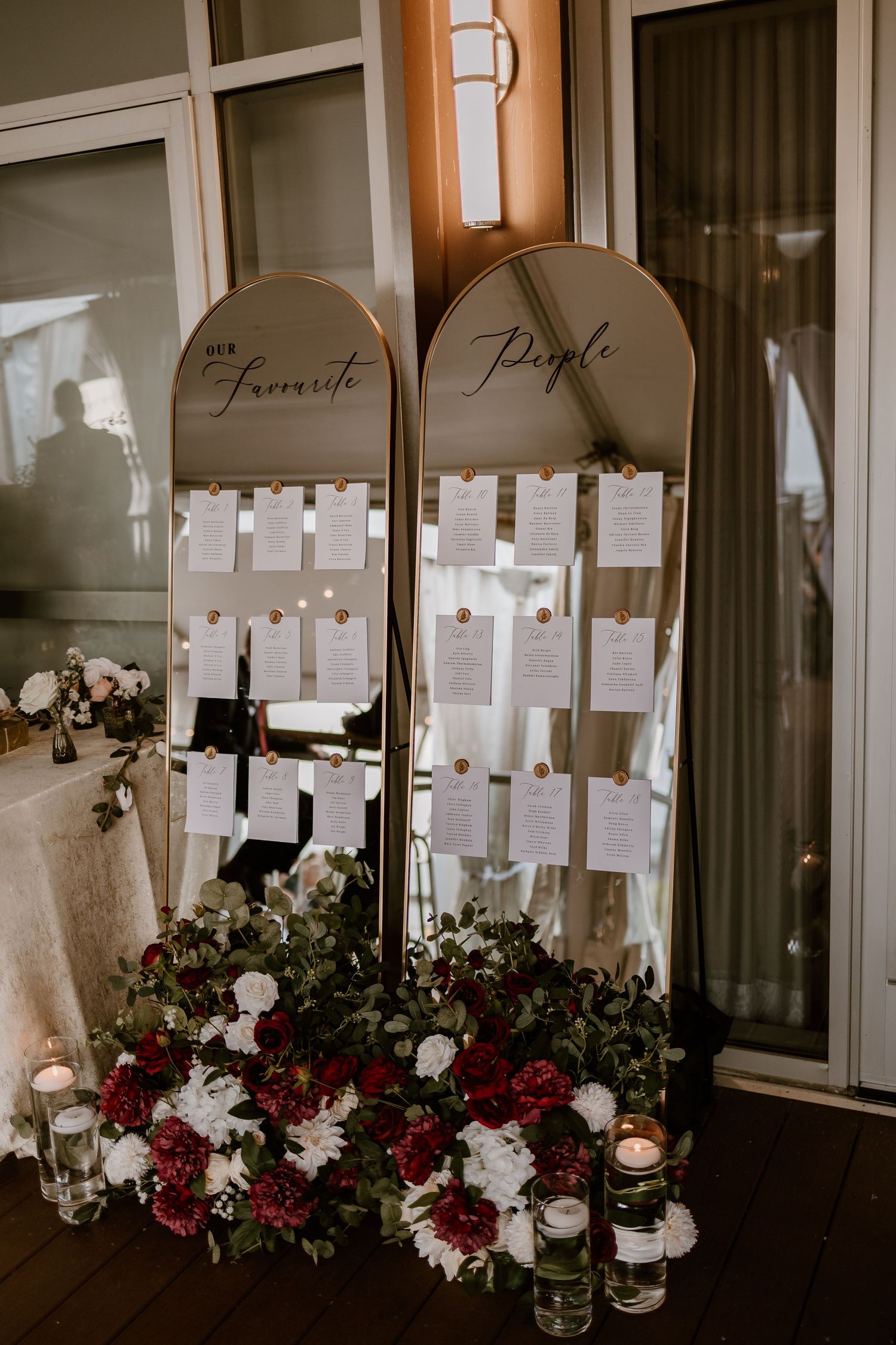 Elegant seating chart display with white cards and burgundy floral arrangements.