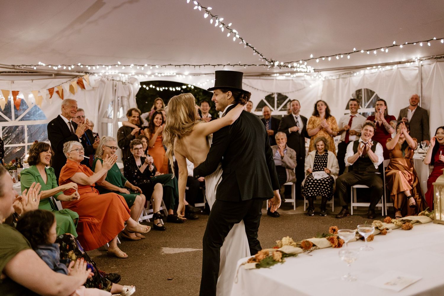 Wedding reception celebration with guests dancing under string lights in a tent.