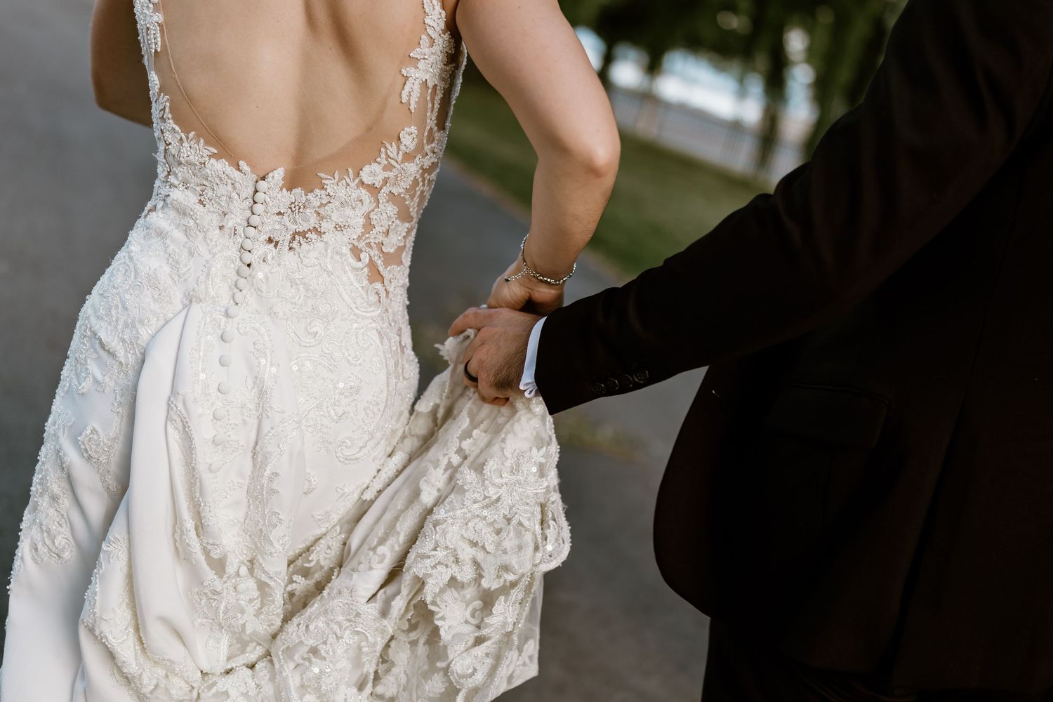 Someone assists with the delicate lace train of a backless wedding dress.