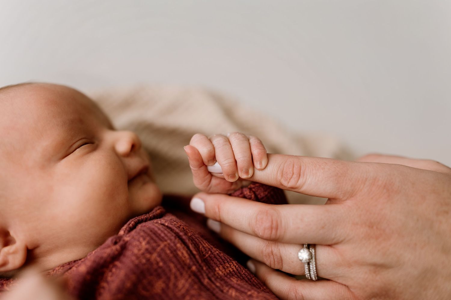 Close-up view of gentle hands cradling sleeping newborn on neutral background.