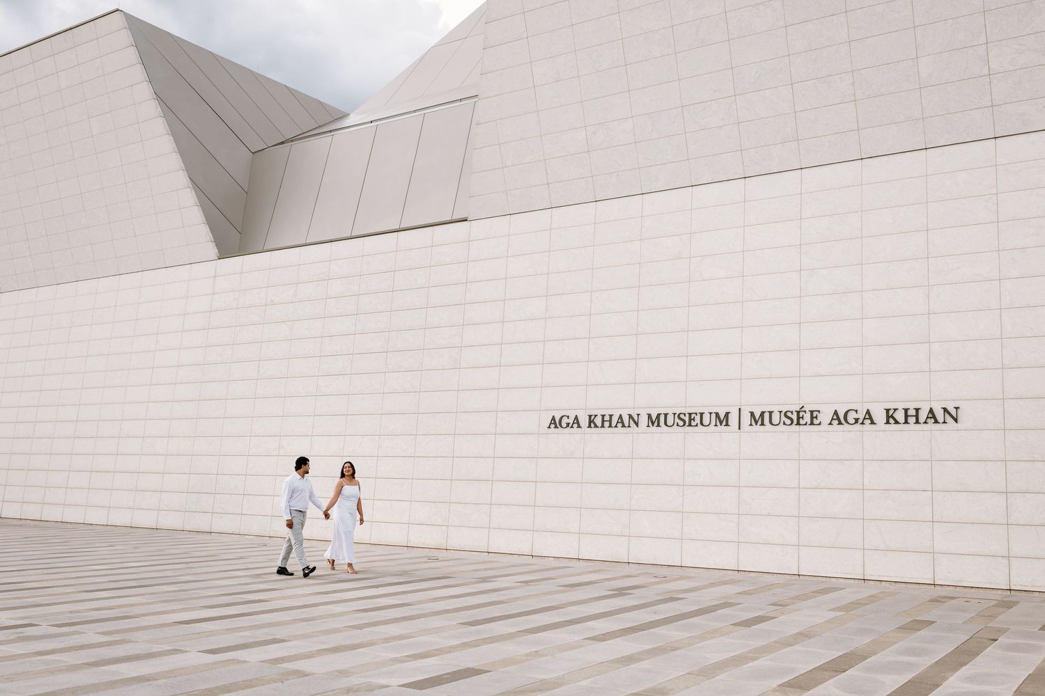 Couple walking outside the Aga Khan Museum, a modern white stone building in Toronto, Canada.