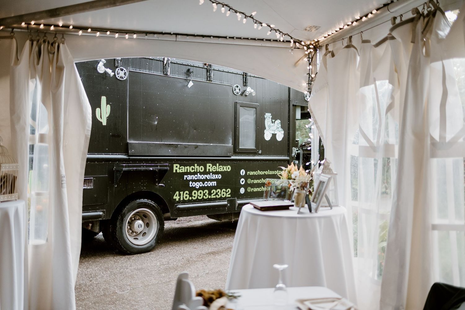 White tent reception space decorated with string lights and elegant table settings.