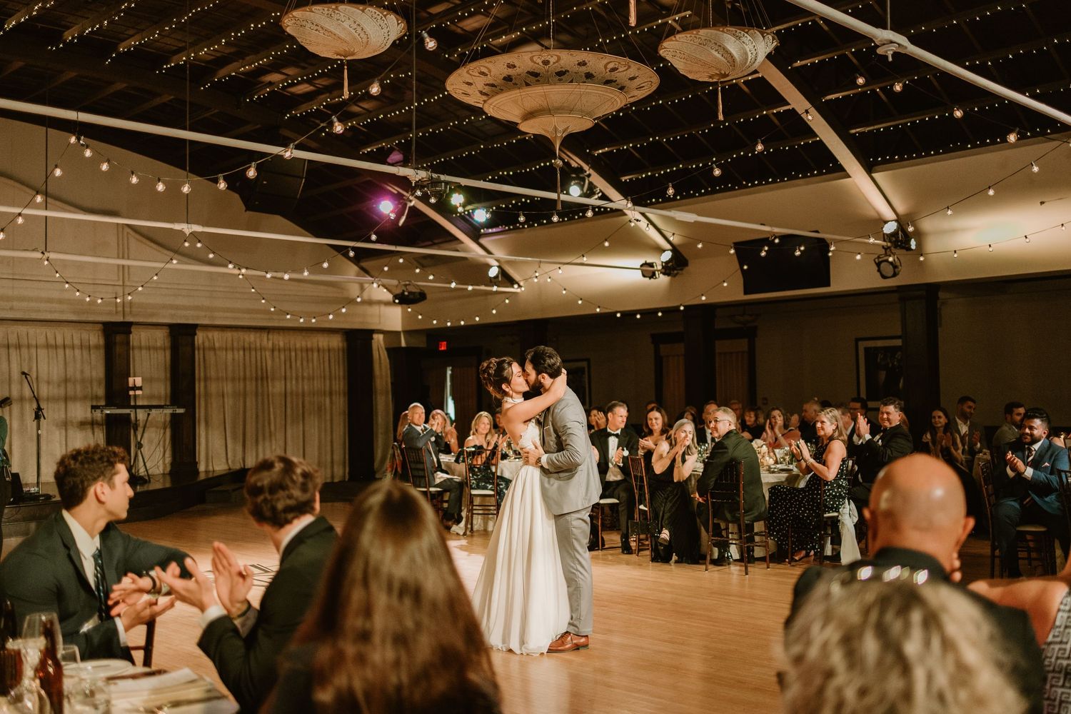 Wedding reception venue with string lights and dance floor filled with celebrating guests.