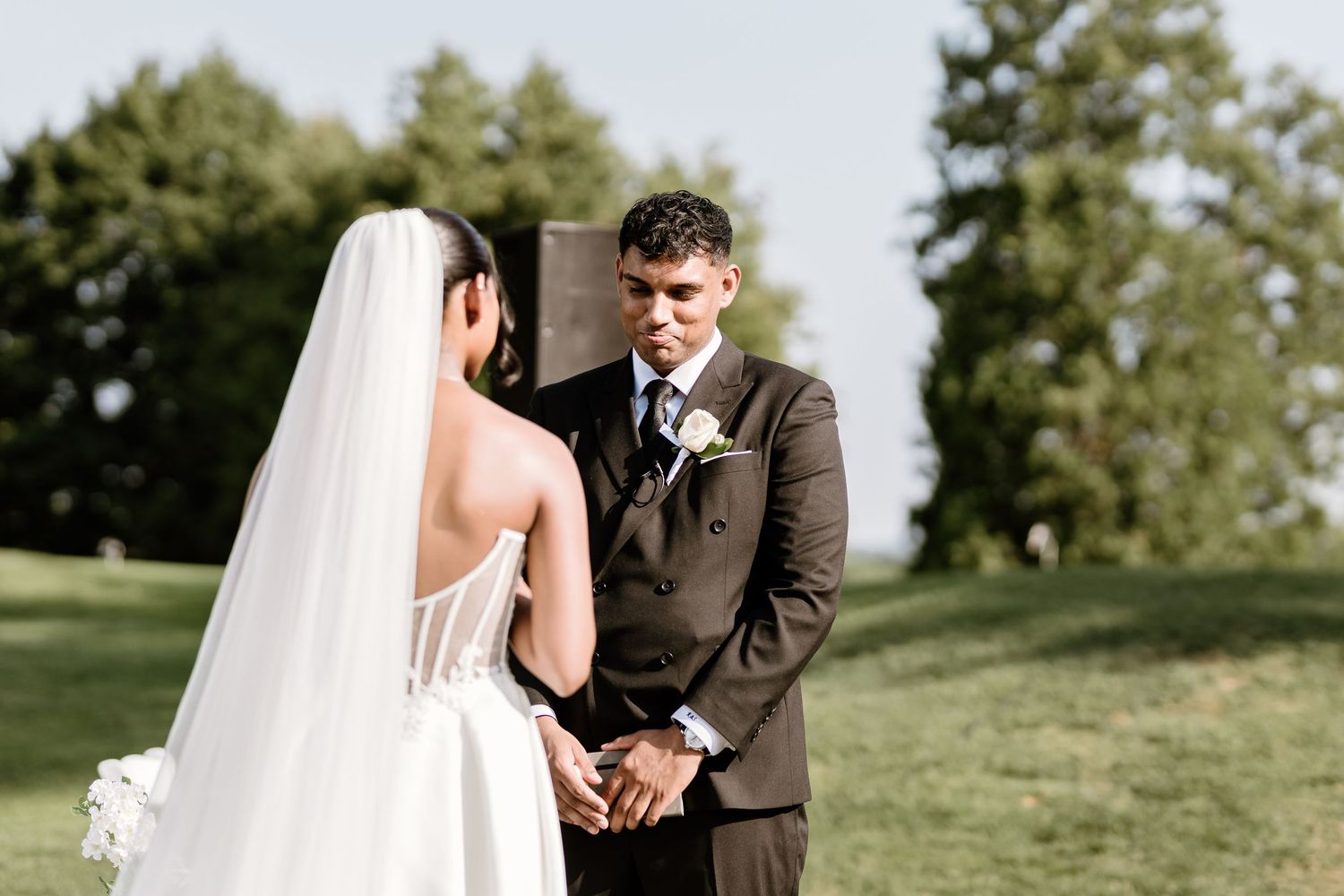 A couple shares an intimate moment during their wedding ceremony on a sunny hillside.