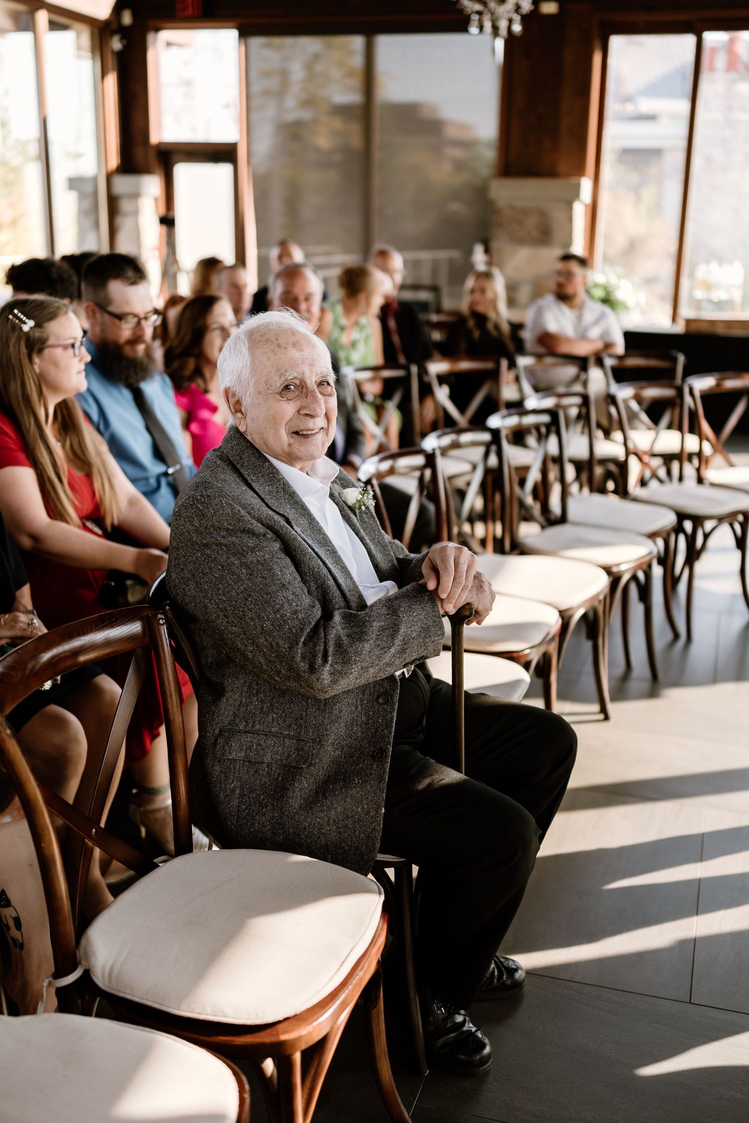 Wedding guest seated in wooden chairs during an indoor ceremony.