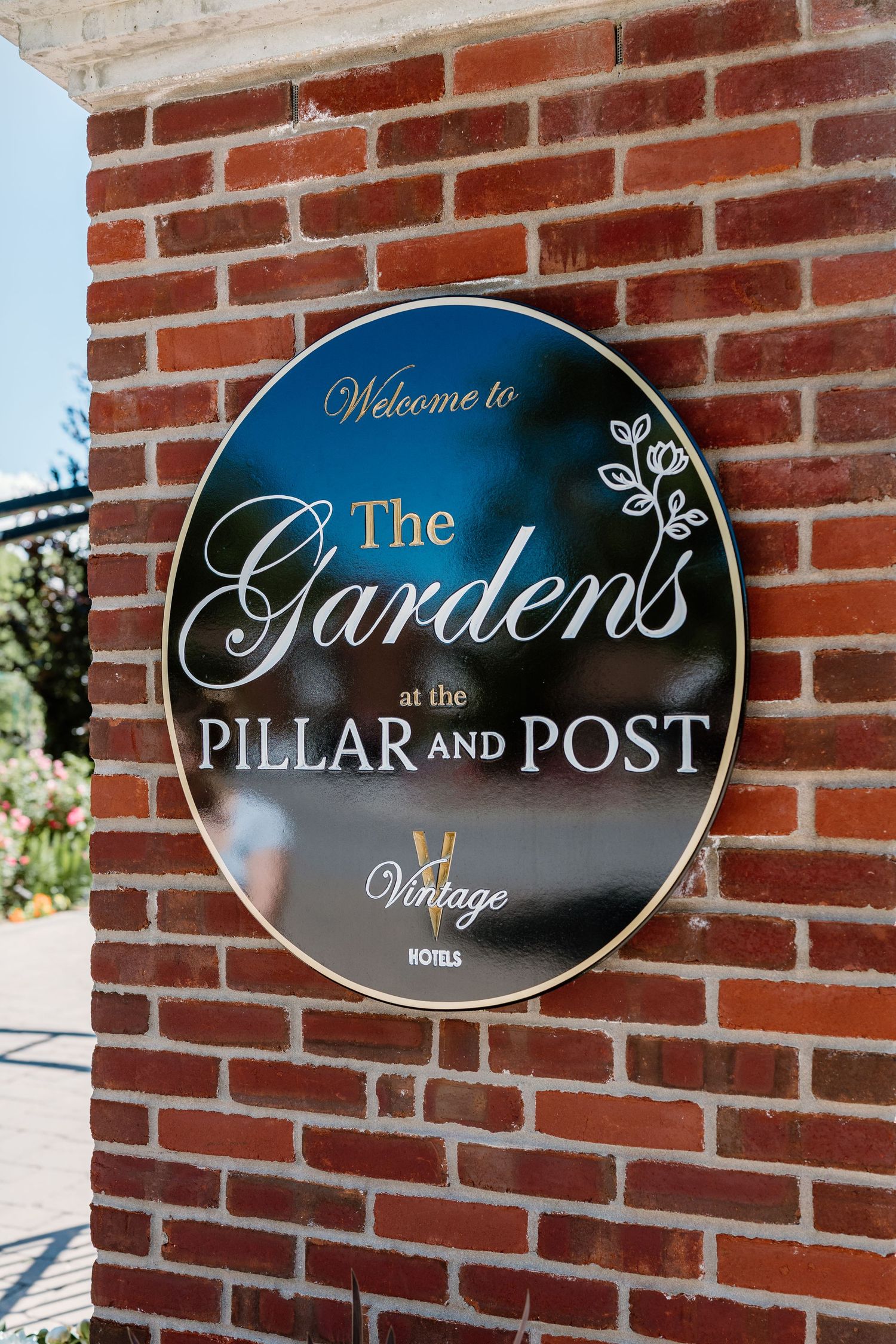 Welcome to The Gardens at the Pillar and Post Vintage Hotels sign on a brick wall.