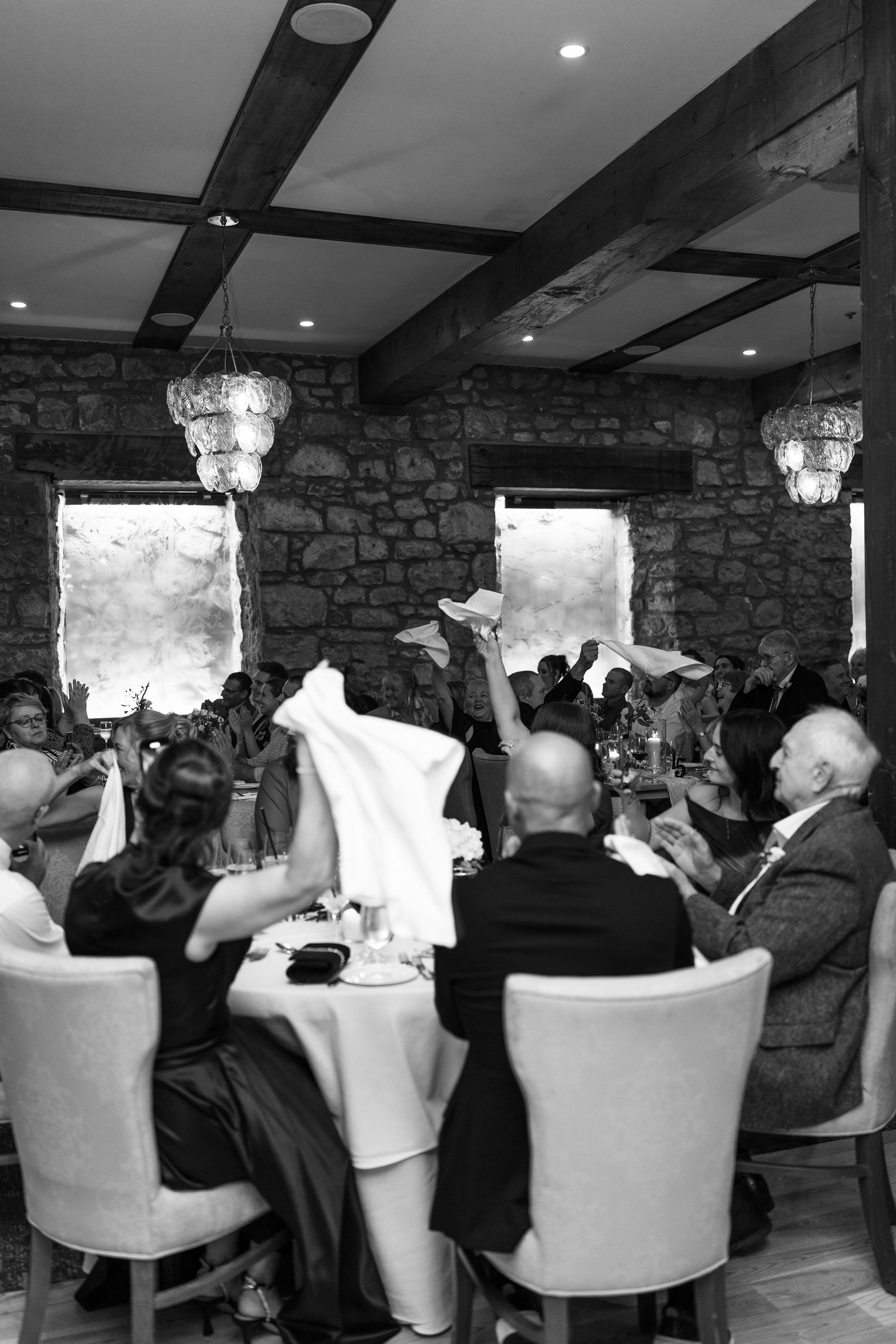 Black and white photo of wedding guests waving napkins during a celebration in an elegant venue.
