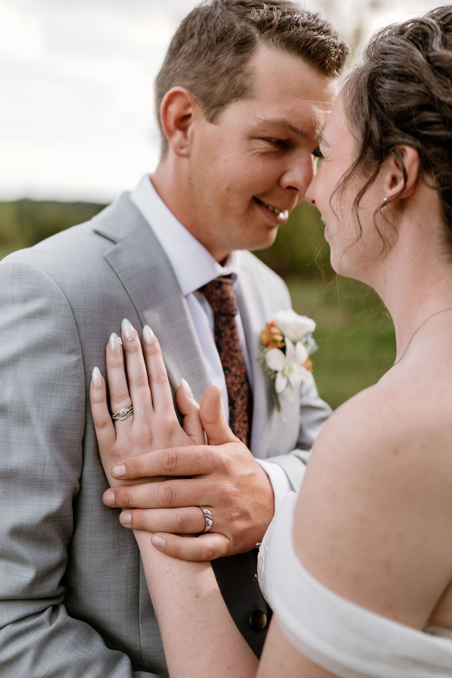 Close-up of newlyweds sharing intimate moment showing wedding rings and formal attire.