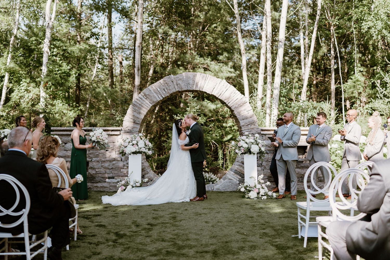 Outdoor wedding ceremony setup with white chairs in a wooded birch grove.