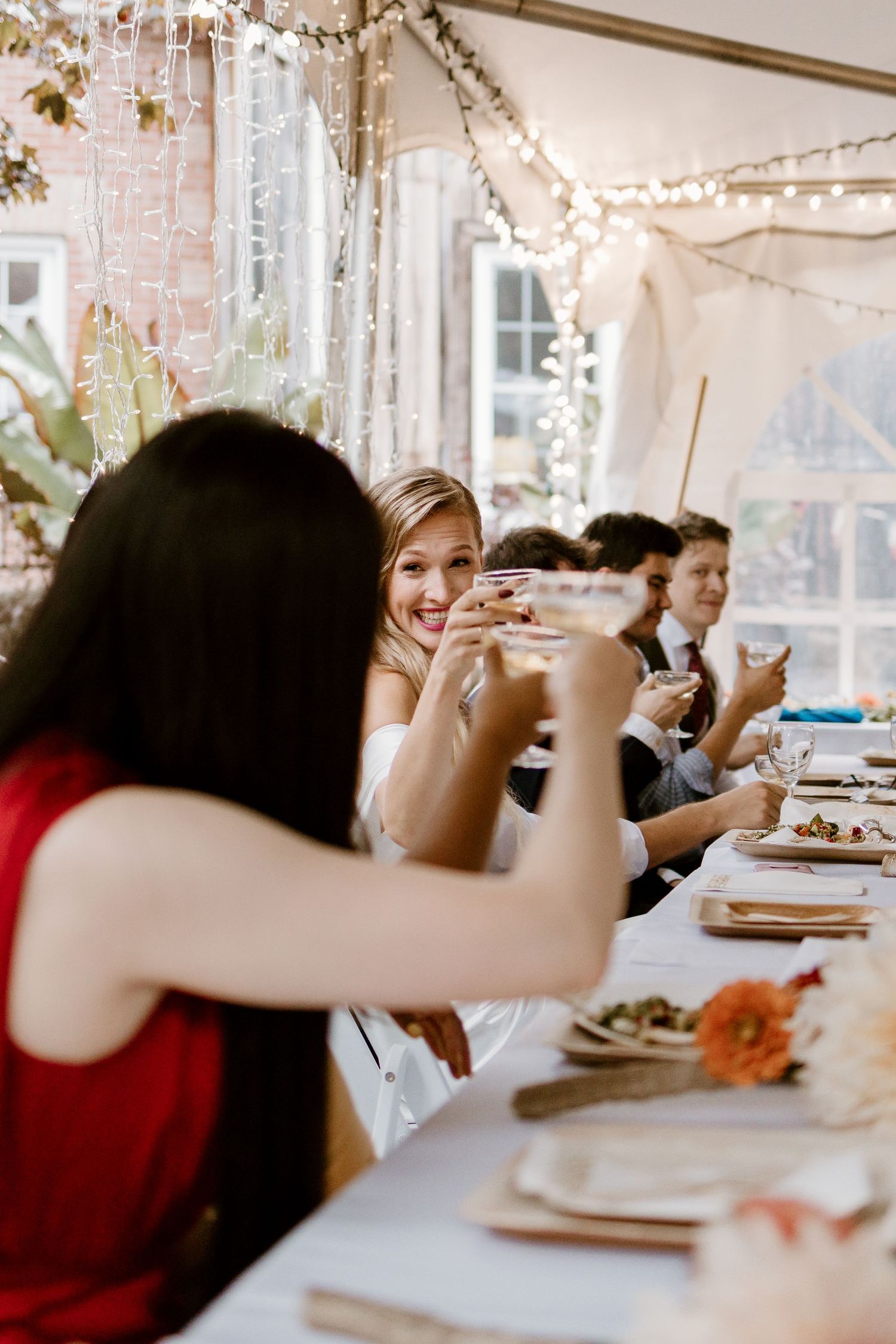 Wedding reception guests raising glasses for a toast under string light decorations.