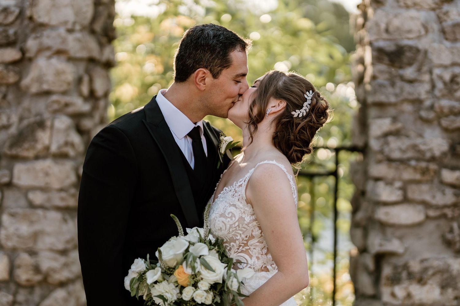 Romantic wedding portrait with couple embracing against stone wall background.