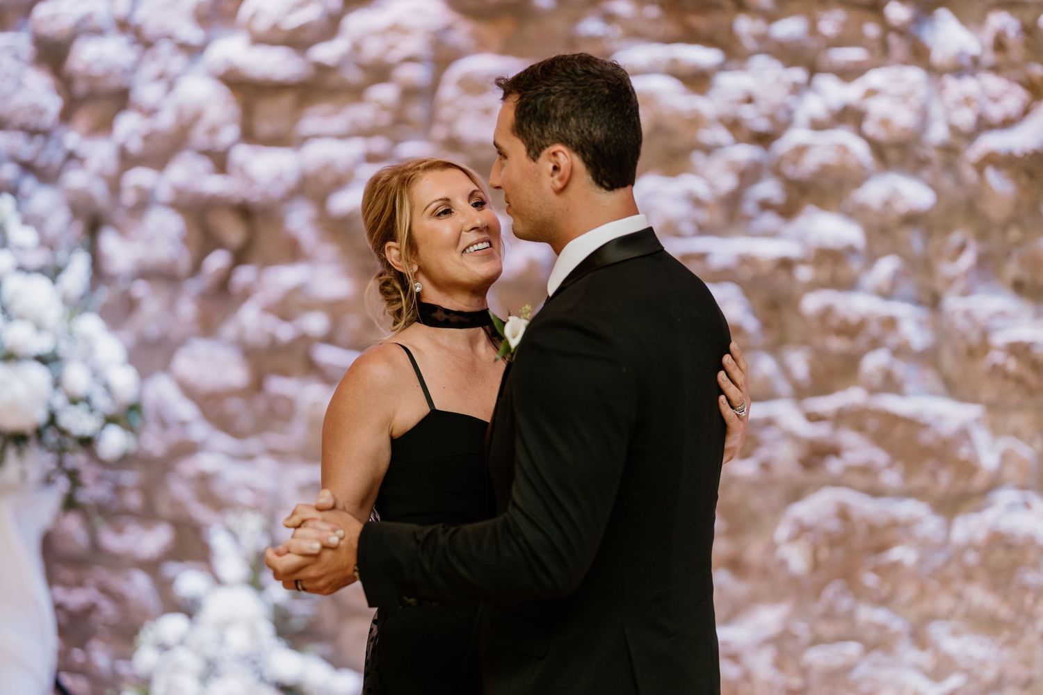 Couples slow dancing at an elegant wedding reception with soft lighting and stone walls.
