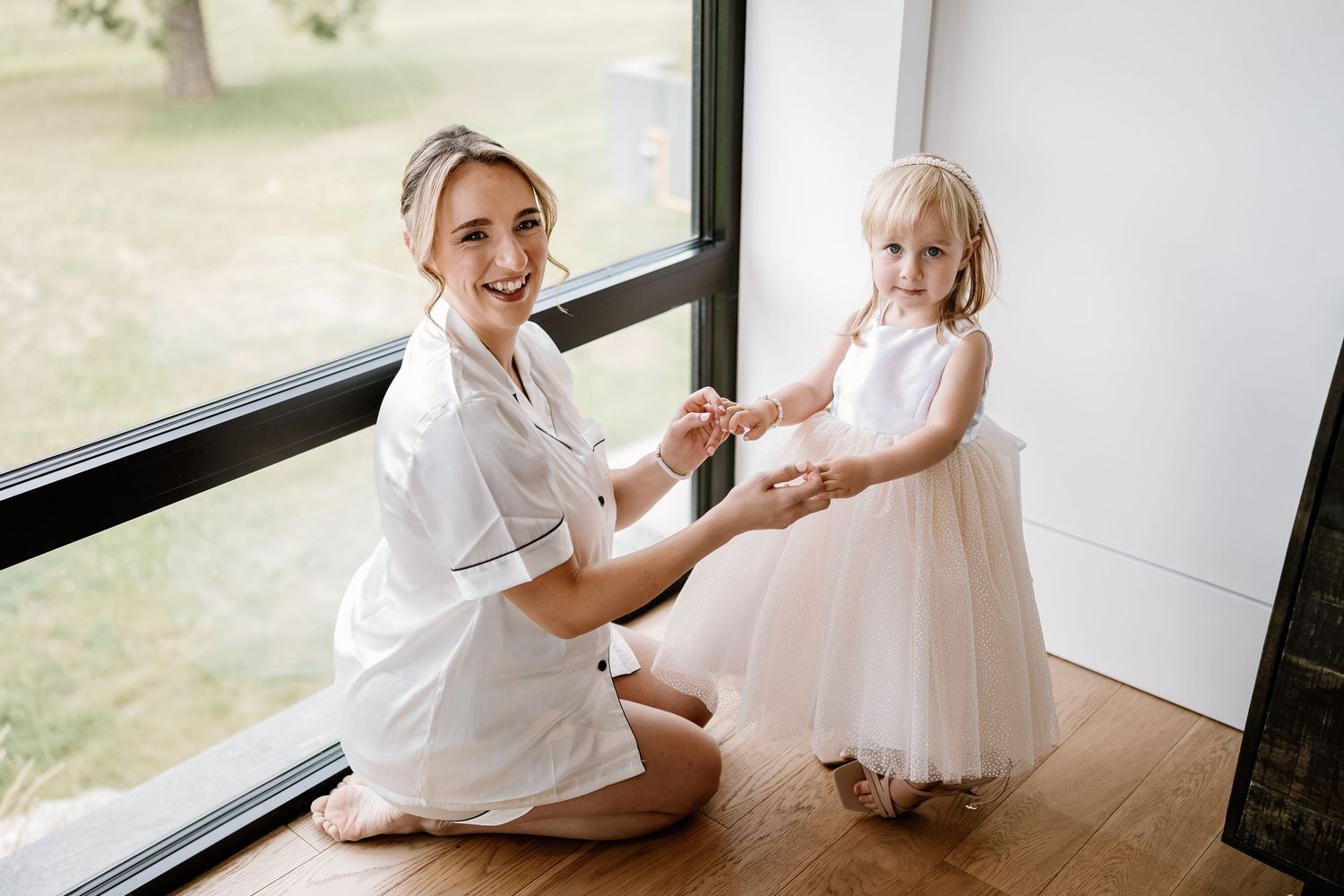 A touching moment during wedding preparations by a large window.