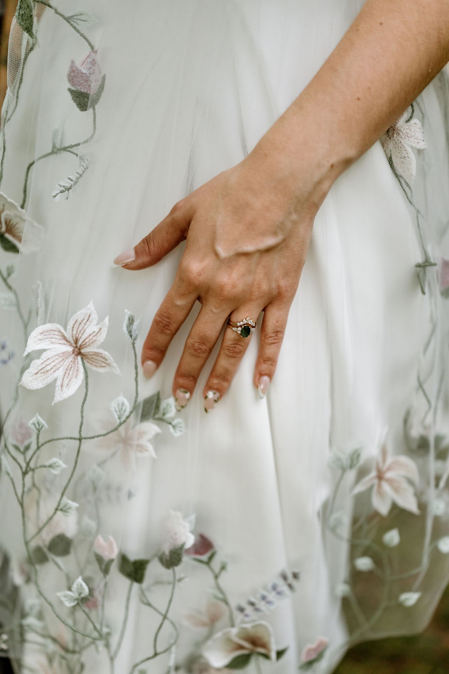 Close-up of wedding ring on hand against floral embroidered dress.