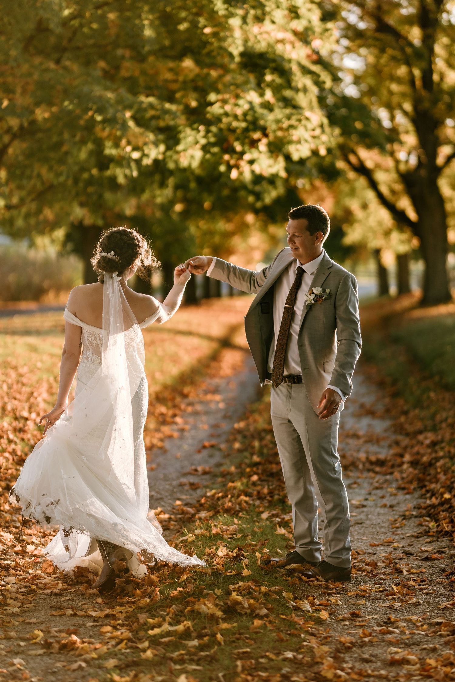 Playful wedding photos in a park with fallen autumn leaves and golden sunlight.