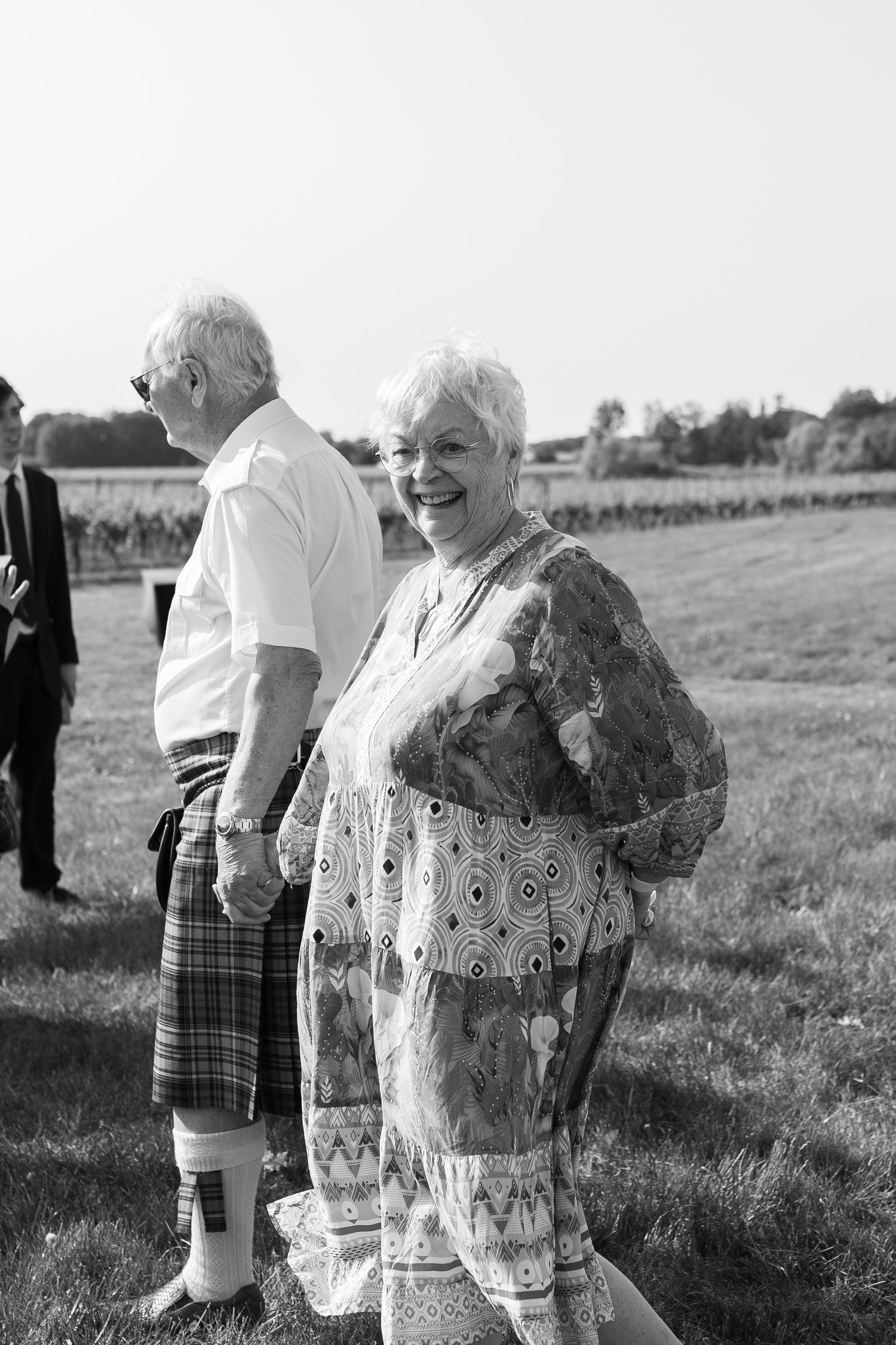 Black and white photo of wedding guests enjoying themselves in a field.