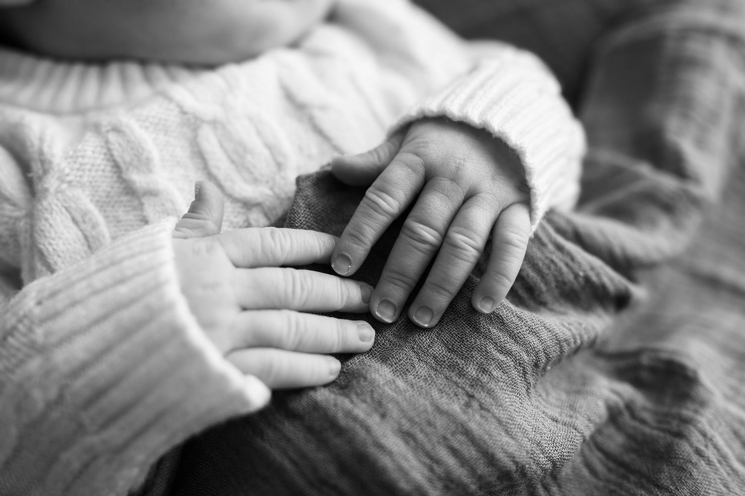 Close-up detail of hands gently touching textured fabric in black and white.