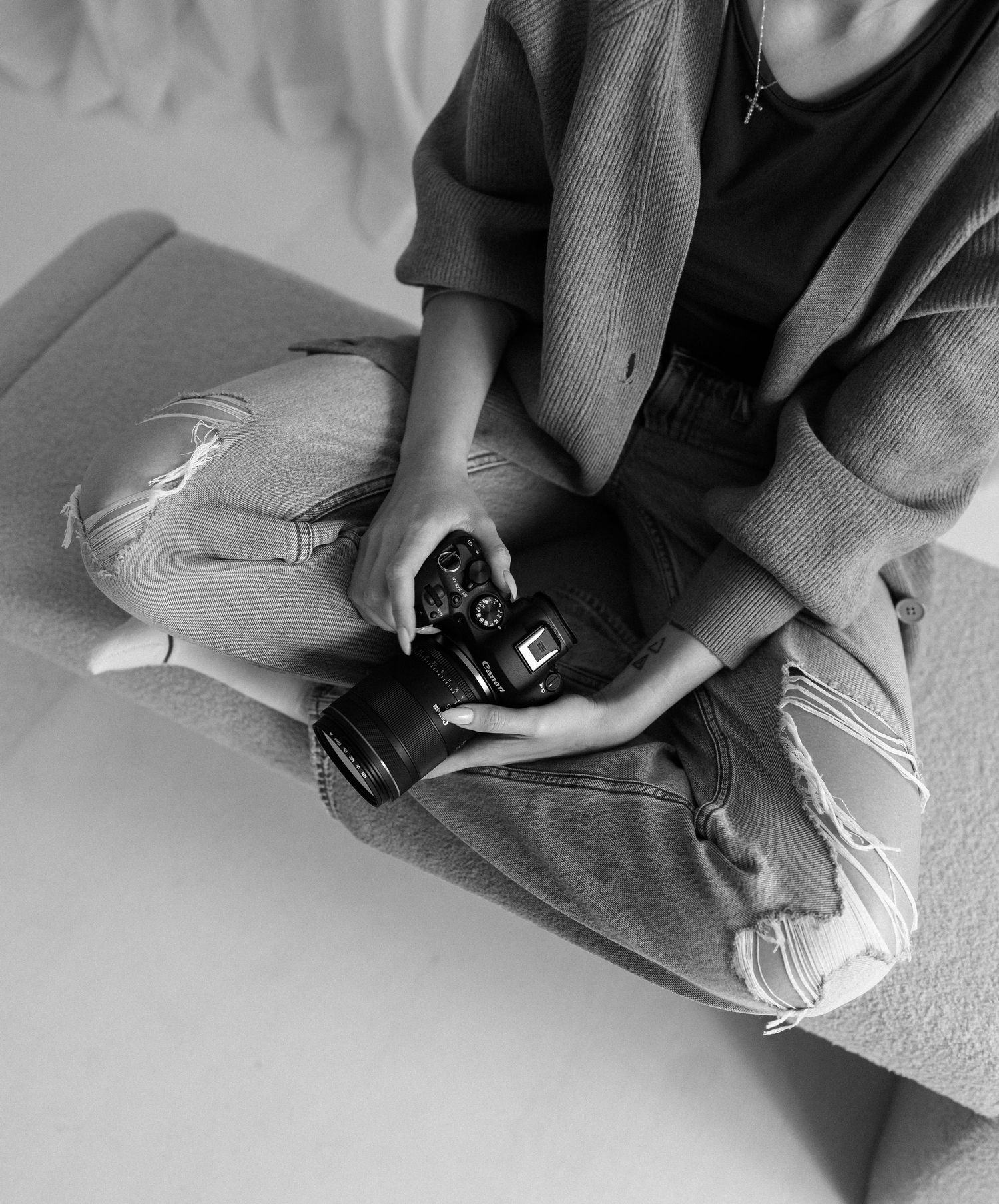 Black and white image of hands holding a vintage camera while sitting on distressed jeans.