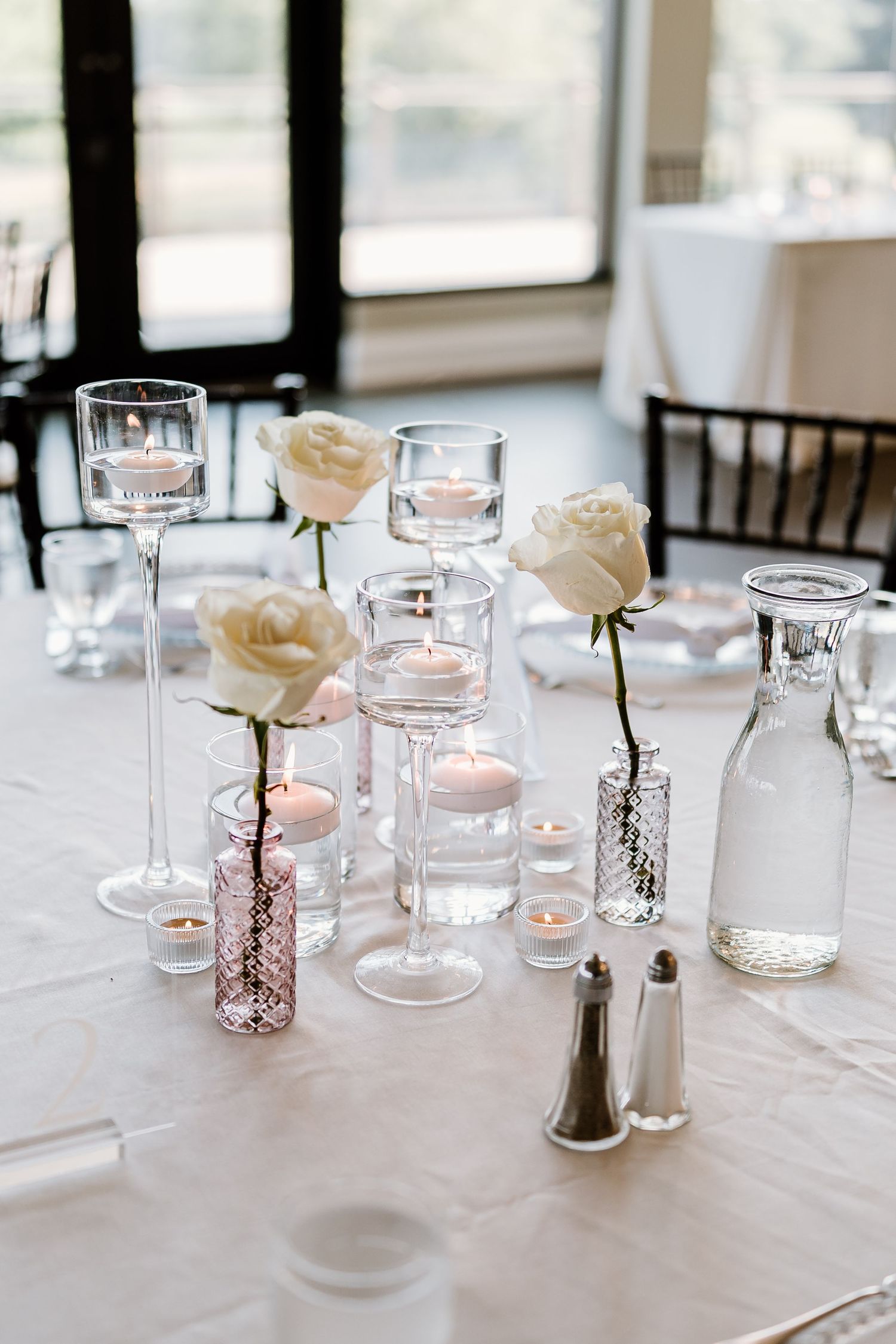 Elegant wedding reception table setting with glass vases, candles and white roses.