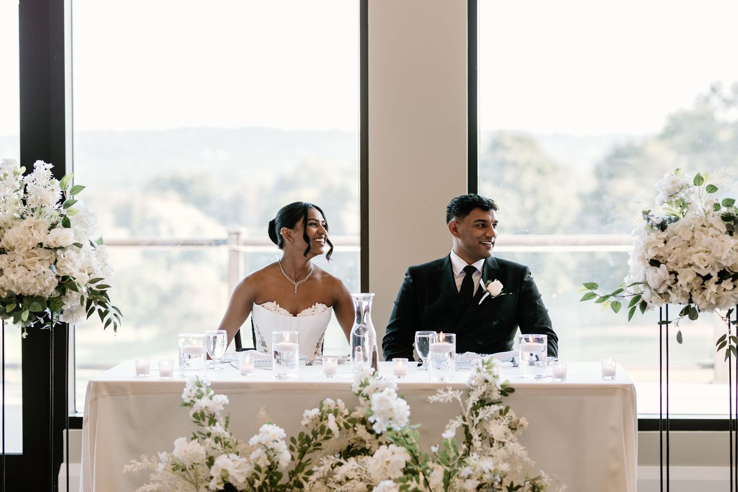A reception table setup with elegant white floral arrangements and large windows.