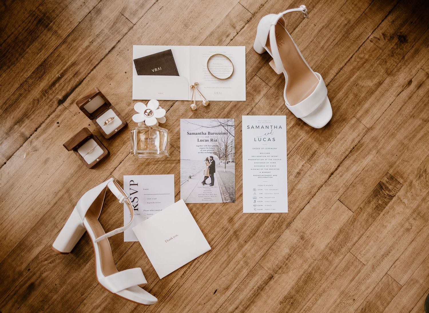 Wedding invitation suite with white heels and stationery on wooden floor.