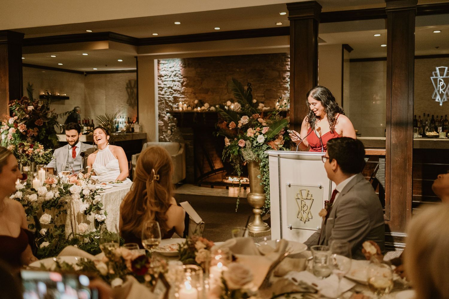 Wedding reception guests gather in an elegant banquet hall with warm lighting and floral centerpieces.