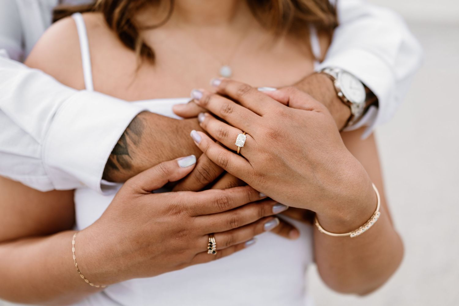 Close-up of couple's hands with gold engagement ring, bracelet, and watch, embracing tenderly.