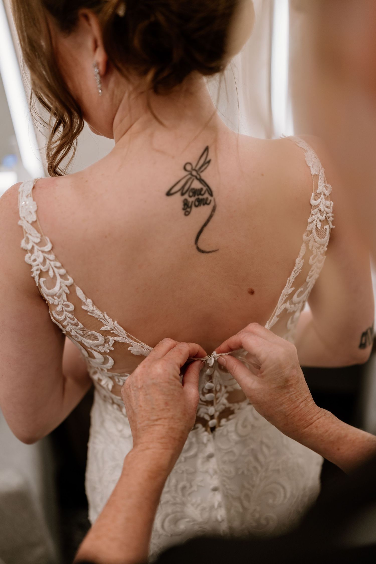 Close-up of hands fastening delicate buttons on a lace wedding gown.