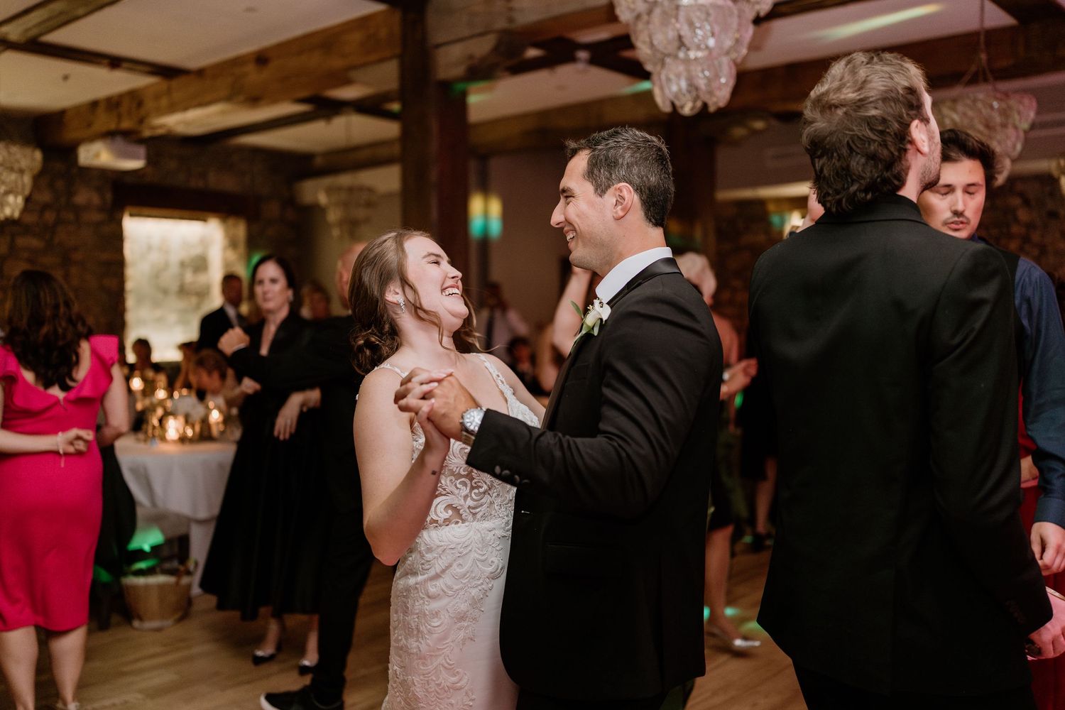 Wedding guests dancing in rustic venue with exposed stone walls and wooden beams.
