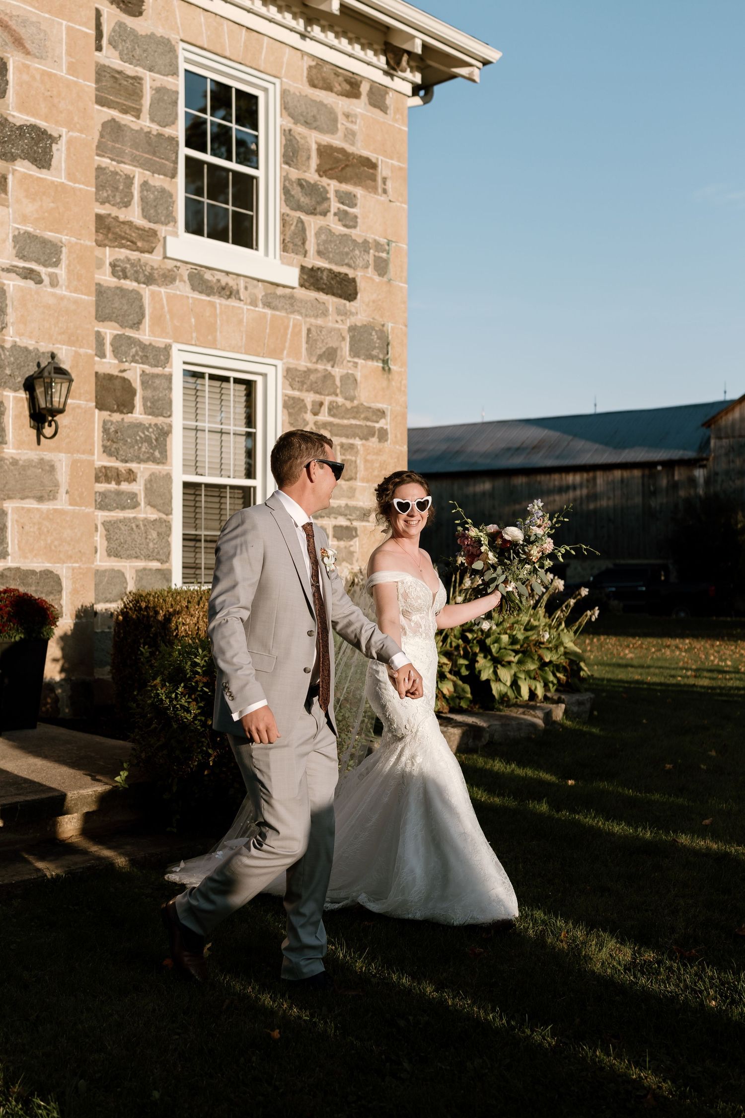 Elegant wedding couple dances outside a stone building during golden hour.