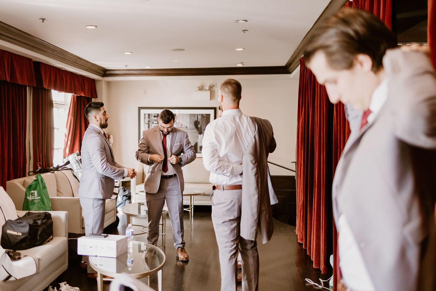 Wedding party members in formal attire gather in hotel suite before ceremony.