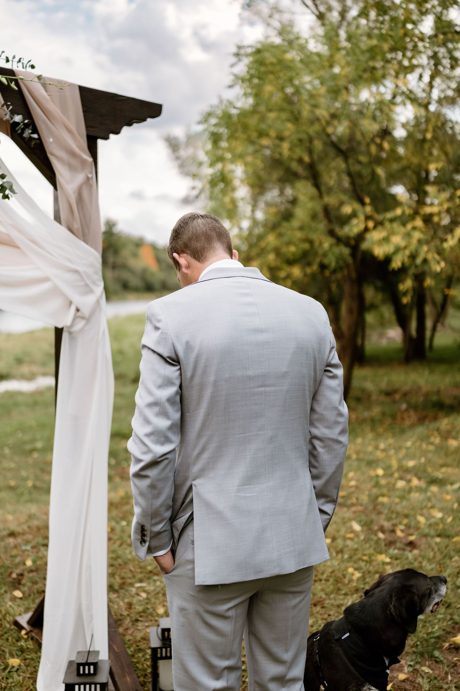A person in a gray suit standing under a decorated wedding arch with fabric draping.