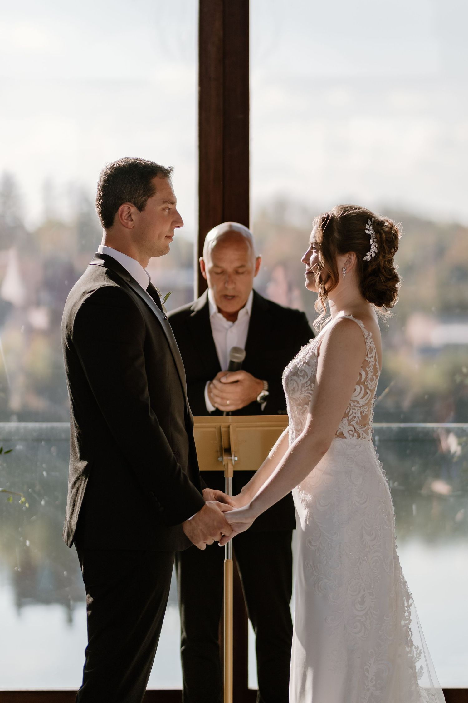 Intimate wedding ceremony taking place by large windows overlooking a scenic waterfront view.