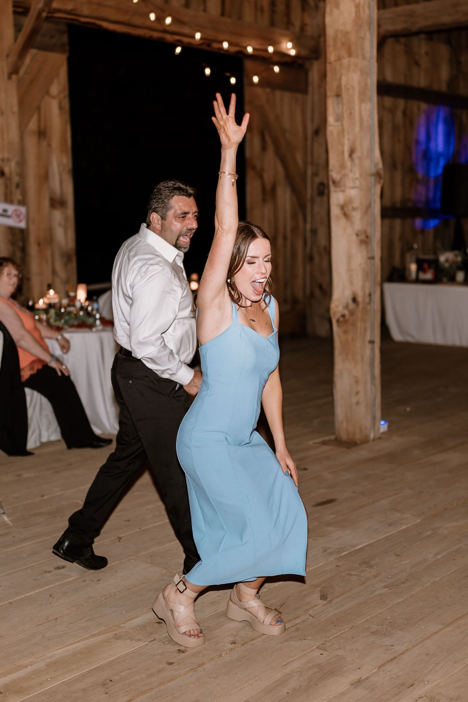 Energetic dance moves captured during a wedding reception on a wooden barn floor.