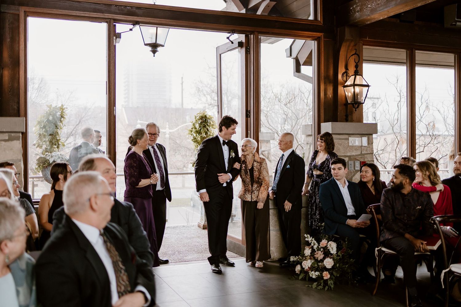 Wedding ceremony in a rustic venue with exposed beams and large windows overlooking a scenic view.