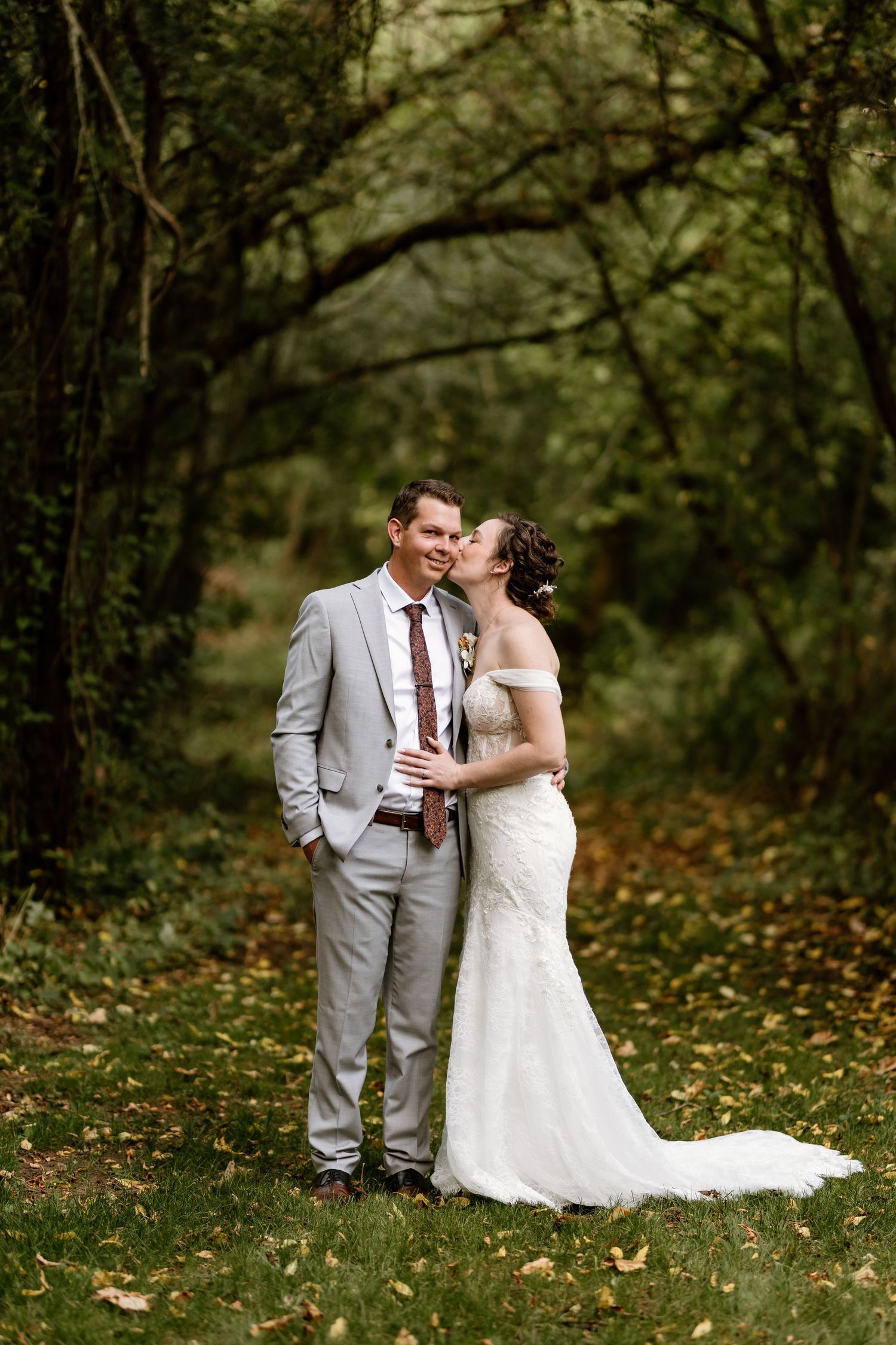 A romantic wedding portrait of a couple embracing in a lush autumn forest setting.