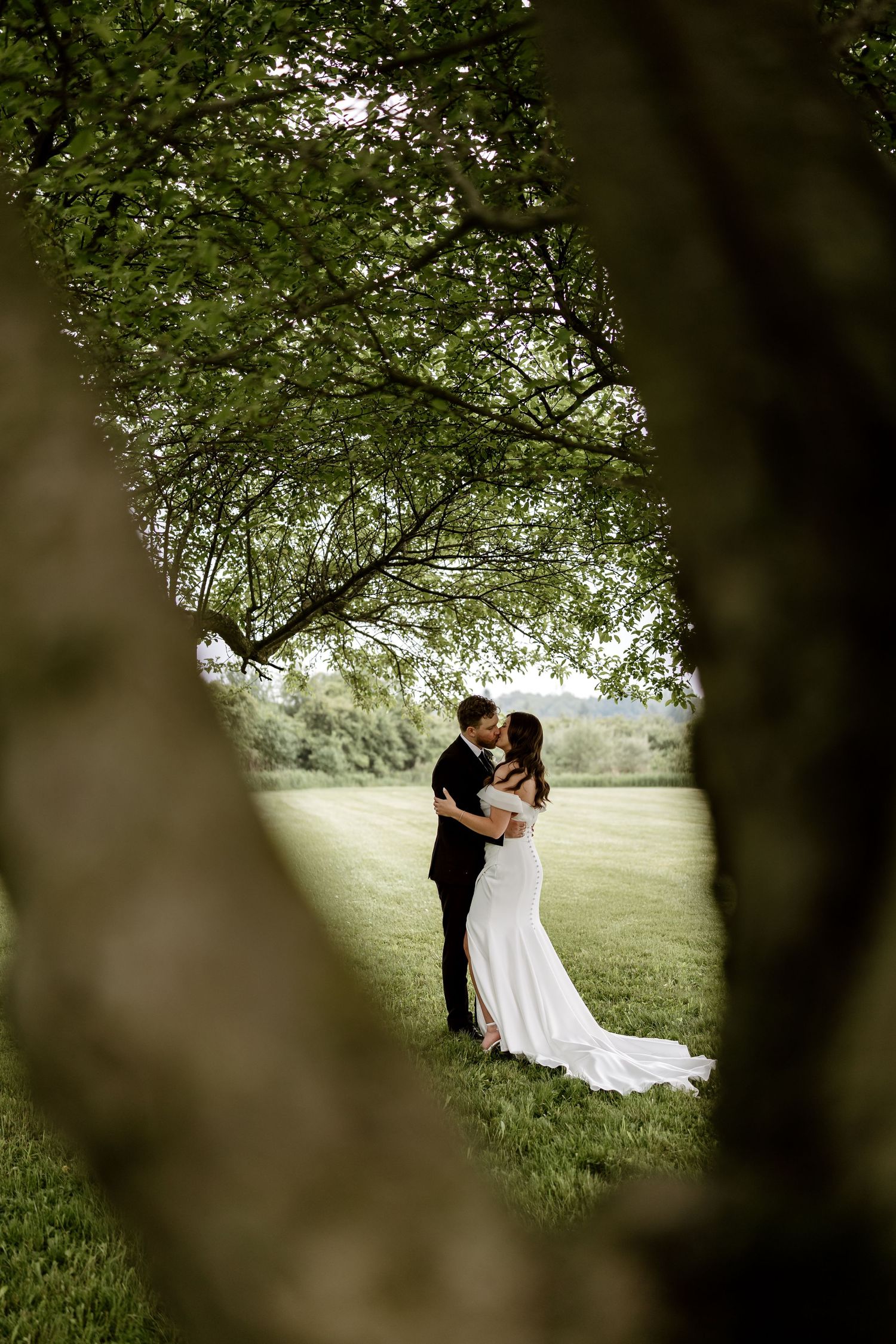 Romantic couple embraces under tree canopy framed by natural greenery.