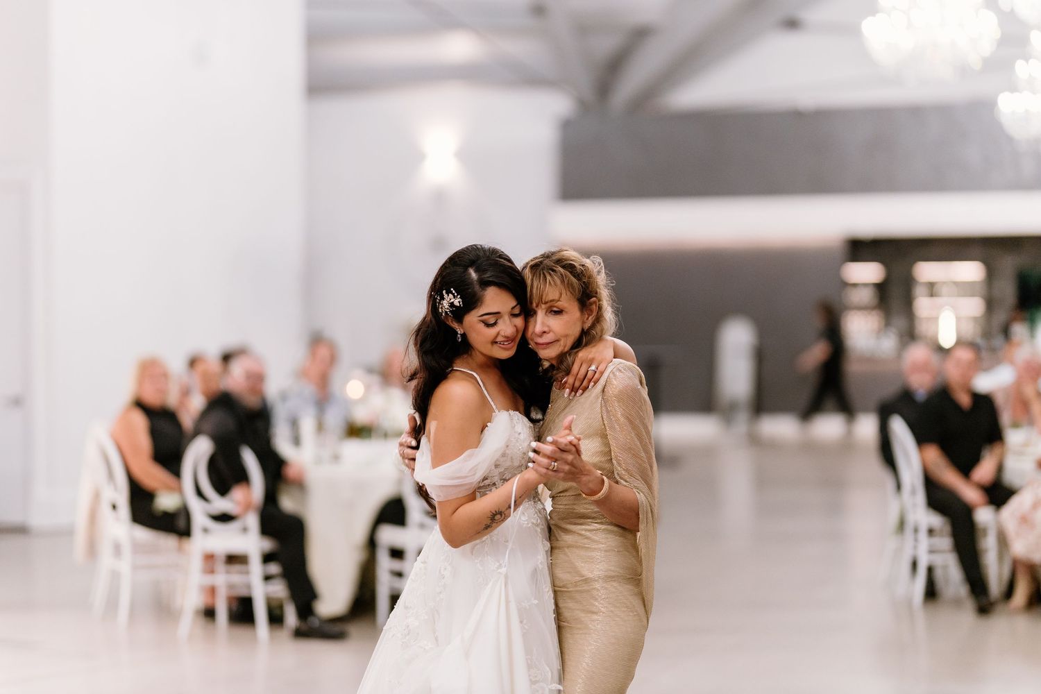 Bride and mother share an emotional dance together in an elegant white wedding reception venue.