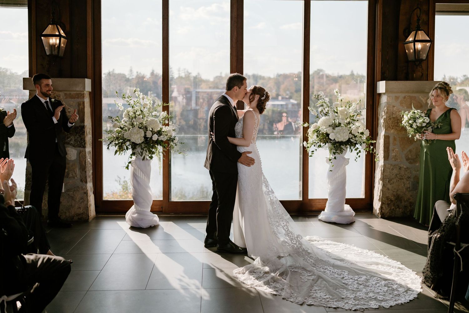 Sunlit indoor wedding venue decorated with floral arrangements and white chairs.