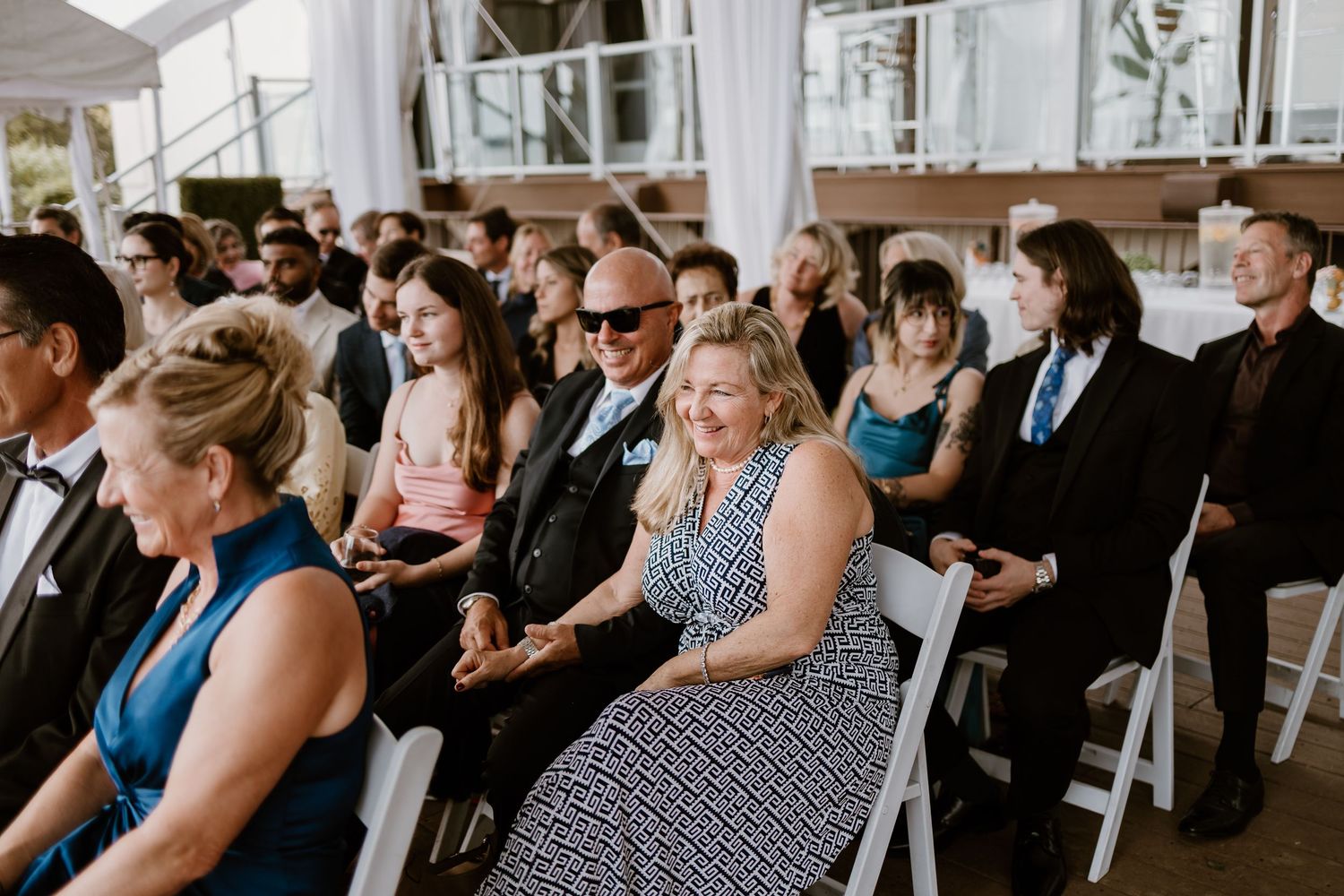 Guests watching a wedding ceremony in a white tent with natural lighting.