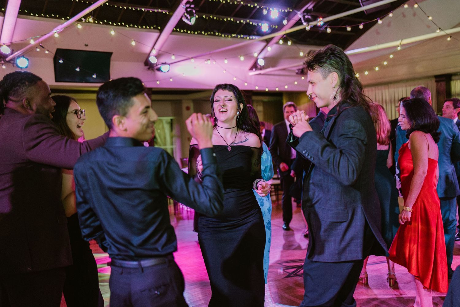 Wedding reception dance floor illuminated with purple lighting and string lights above.