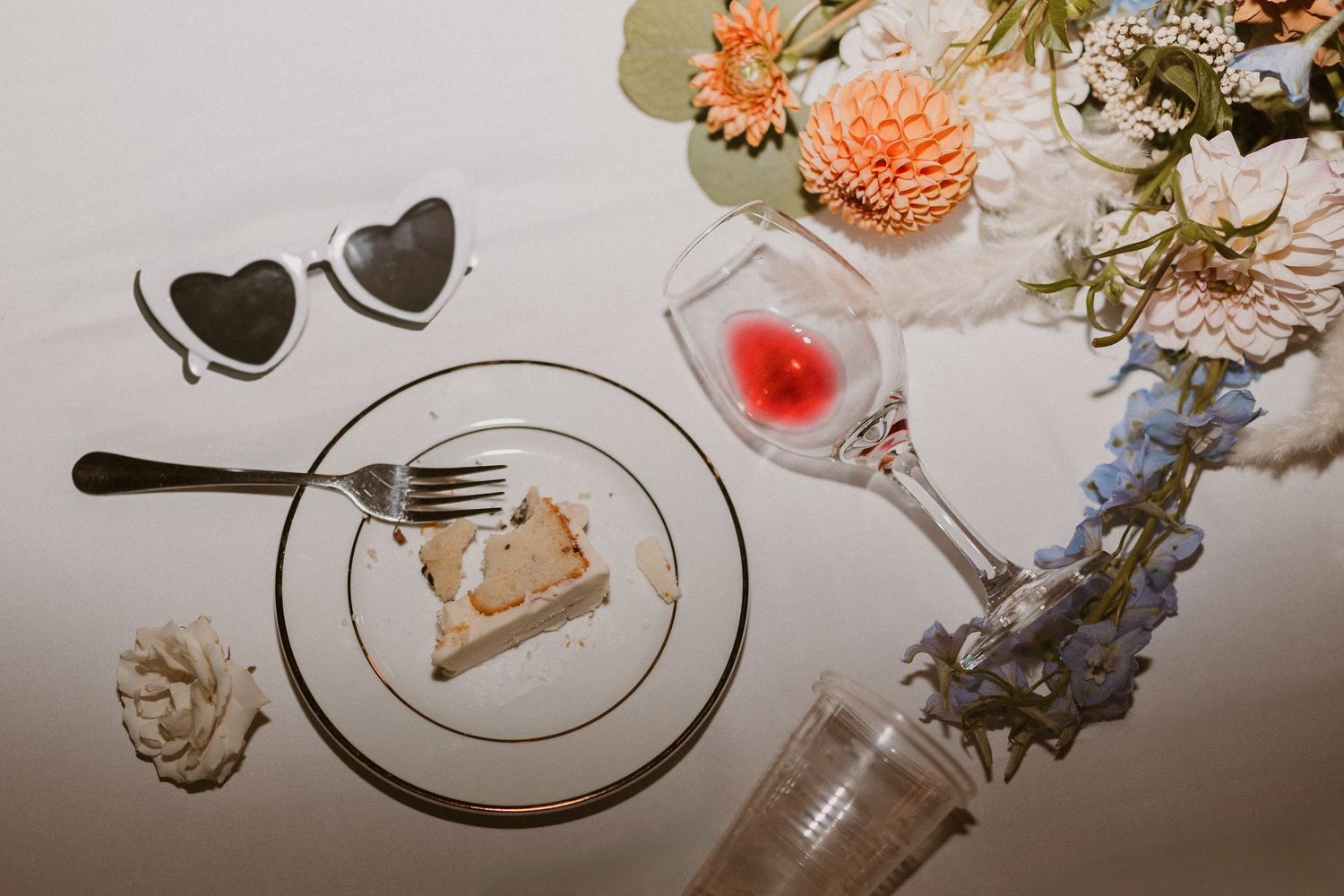 Wedding reception table detail with heart-shaped sunglasses, dessert plate, and floral centerpiece.