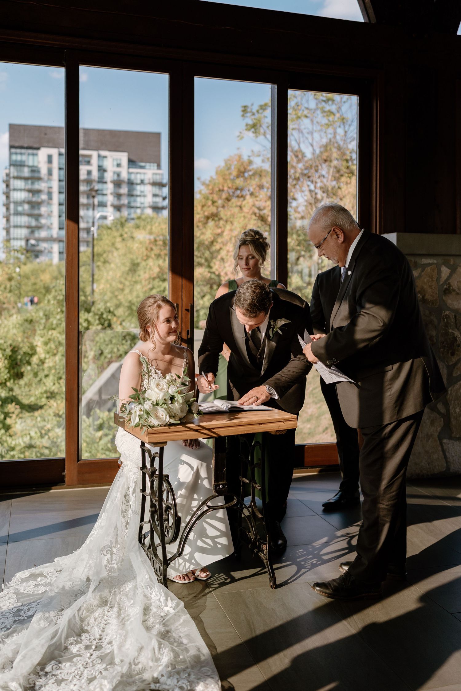 Wedding ceremony in sunlit room with floor-to-ceiling windows overlooking city views.