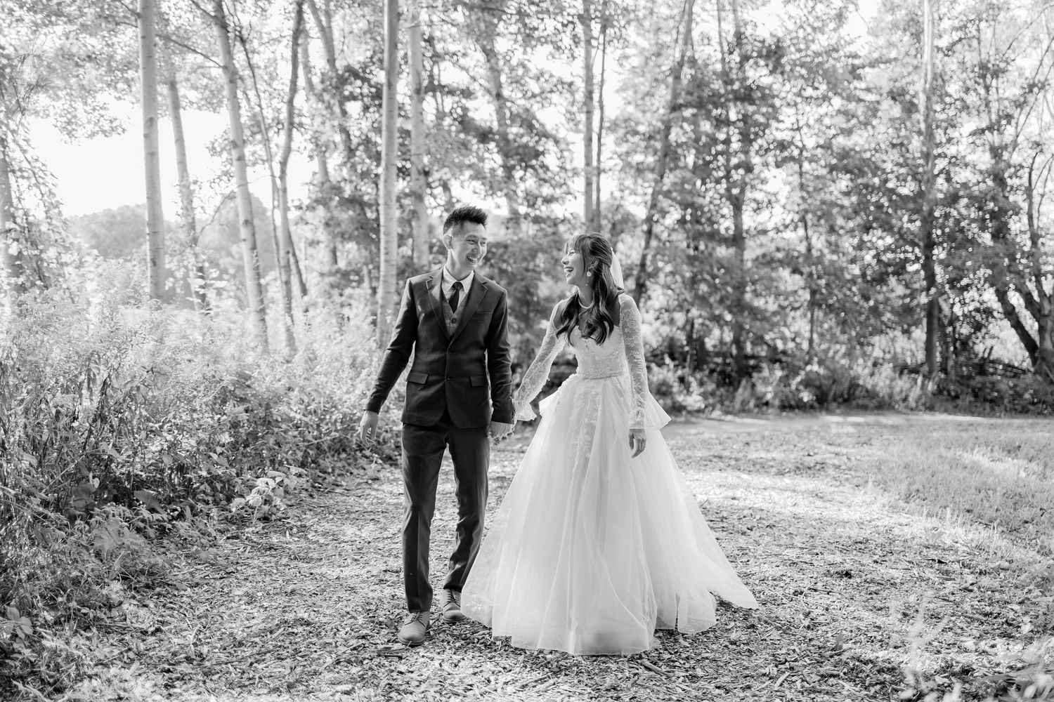A wedding party walking through a sunlit wooded area in formal attire.