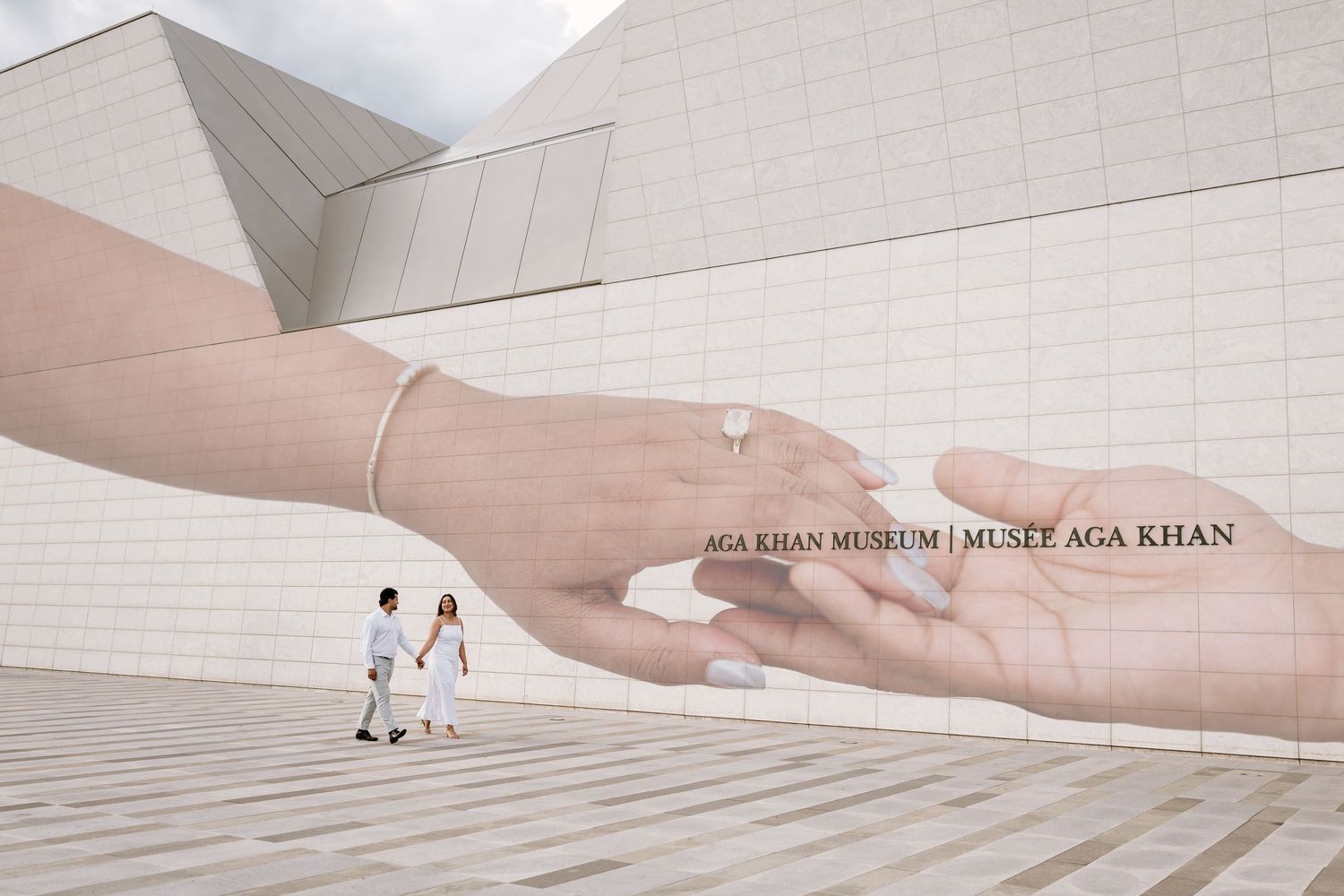 Couple walks past large mural of hands at Aga Khan Museum in Toronto, Canada.