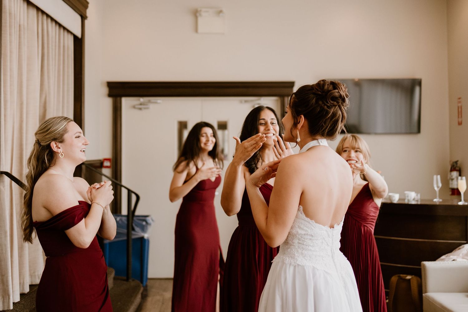Wedding party in burgundy dresses laughing together during pre-ceremony preparations.